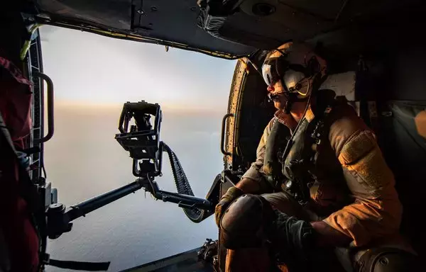 أحد أفراد الأطقم الجوية بالبحرية الأميركية يوفر الأمن من مروحية من طراز إم إتش-60أر سي هوك. [القيادة المركزية الأميركية]