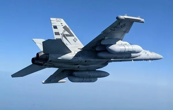 A Next Generation Jammer Mid-Band flies on an EA-18G Growler (forward pod under the right wing of the aircraft). [US Navy]